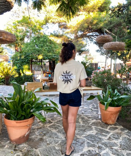 Mujer con camiseta beige y shorts caminando en un jardín.